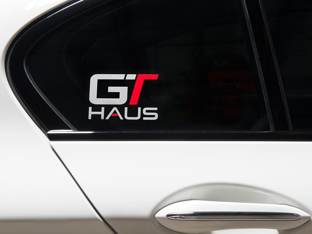 GTHAUS decal featuring bold red and gray lettering on a transparent background, applied to a car window.