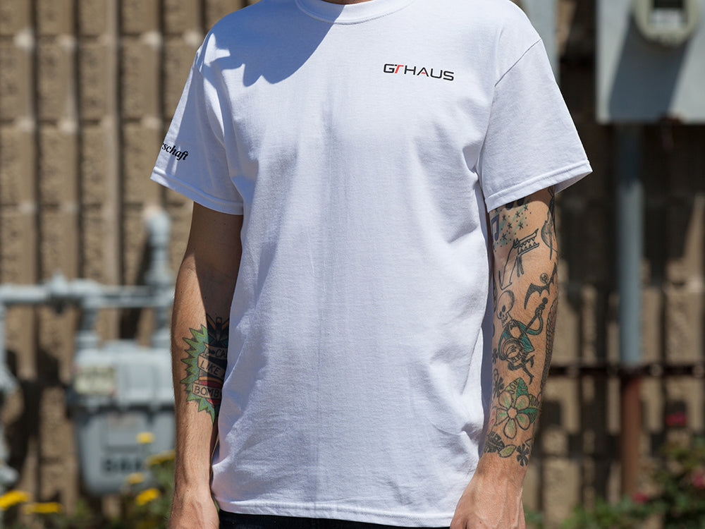 White GTHAUS T-shirt displayed on a person, featuring the GTHAUS logo on the front and tattoos visible on the arms.
