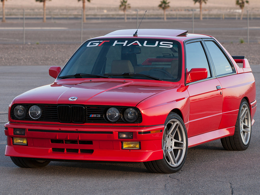 GTHAUS decal on a BMW M3 front windshield, showcasing a sleek design against a vibrant red car.