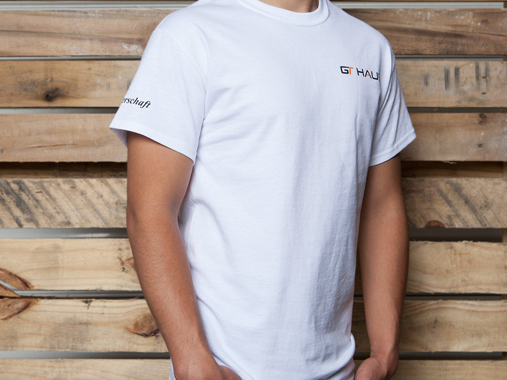 GTHAUS white T-shirt featuring the logo on the front and Meisterschaft branding on the sleeve.