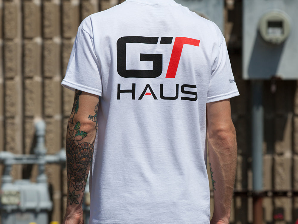 White GTHAUS T-shirt featuring bold black and red logo on the back, showcasing a sporty design for automotive enthusiasts.